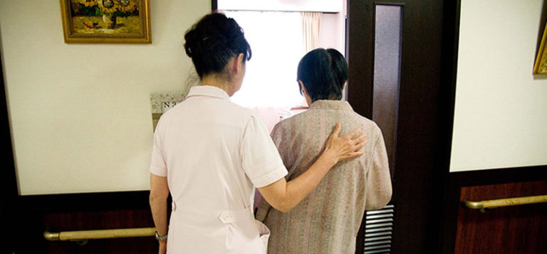 介護職員が入居者をサポートしながら歩行介助している風景